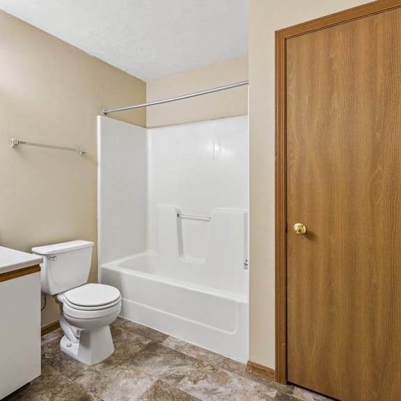 Thumbnail 12 of 16 Apartment bathroom with a single-sink vanity, large mirror, toilet, tub/shower combination, and durable flooring with neutral finishes throughout.