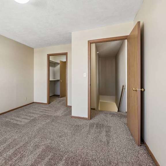 Thumbnail 7 of 16 Spacious apartment bedroom with neutral carpet, beige walls, wood-trimmed doors, and an open layout leading to the hallway and closet area.