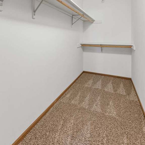 Thumbnail 11 of 16 Walk-in apartment closet with carpeted flooring, wraparound hanging rods, upper shelving, and an attic access panel for additional storage.