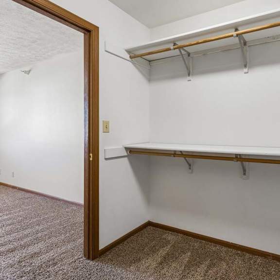 Thumbnail 10 of 16 Walk-in apartment closet with carpeted flooring, dual hanging rods, upper shelving, and an open doorway connecting to the adjacent bedroom.