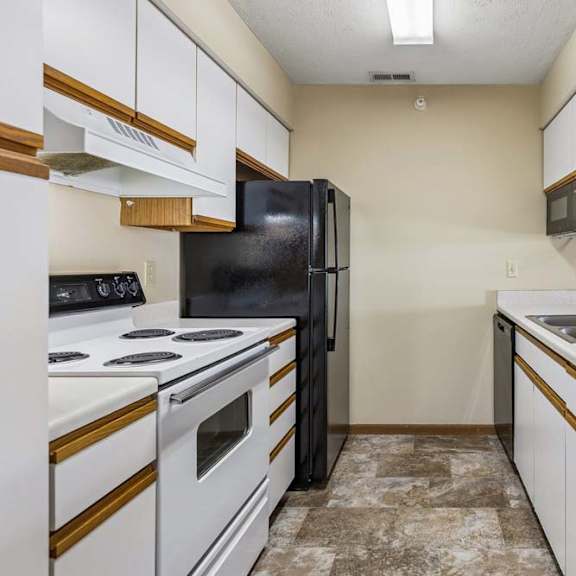 Thumbnail 2 of 16 Galley-style apartment kitchen with white cabinets, white oven, black refrigerator, laminate countertops, a double-basin sink, and durable flooring in a functional layout.