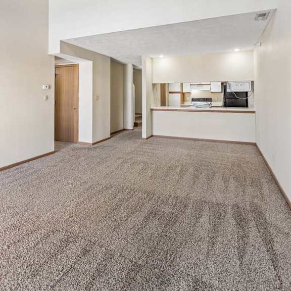 Thumbnail 4 of 16 Spacious apartment living room with vaulted ceilings, neutral carpet, and an open-concept layout featuring a breakfast bar overlooking the kitchen.