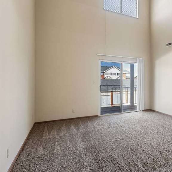 Thumbnail 5 of 16 Spacious apartment living room with vaulted ceilings, neutral carpet, and a large sliding glass door with a transom window that fills the space with natural light.