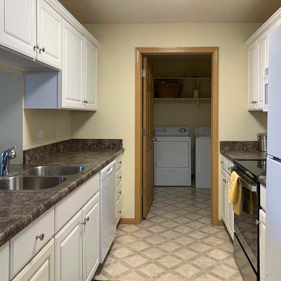 Thumbnail 17 of 20 a kitchen with white cabinets, dark counter tops, vinyl flooring, and a white fridge