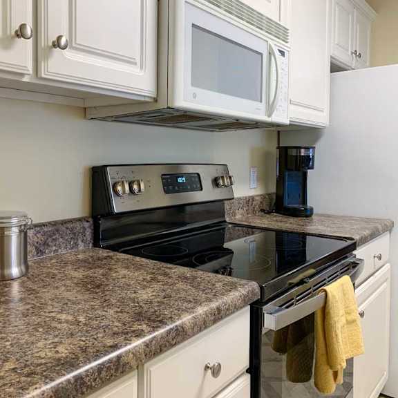 Thumbnail 19 of 20 a kitchen with white cabinets, dark grey countertops, a white microwave and glass top stove
