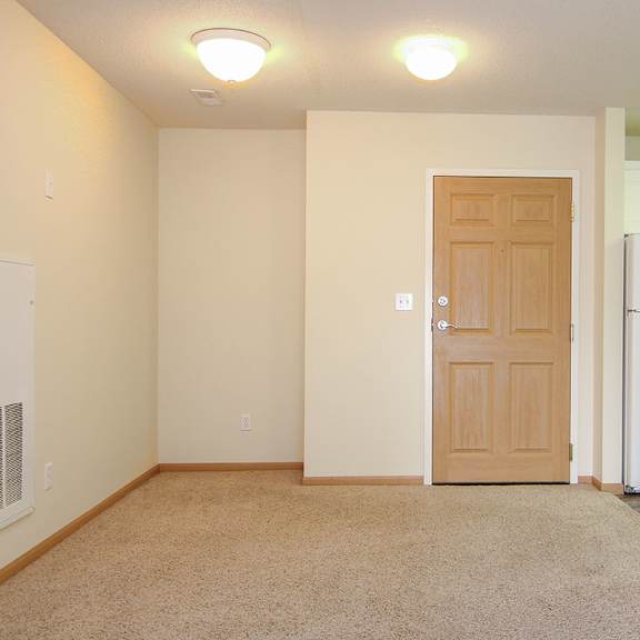 Thumbnail 8 of 12 A room with a brown door and a white refrigerator in the background.