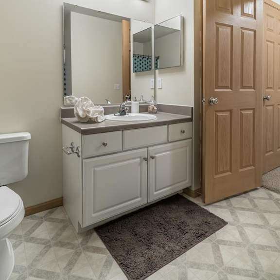 Thumbnail 13 of 20 A bathroom with a white toilet, a sink with a mirror above it, and a brown door.