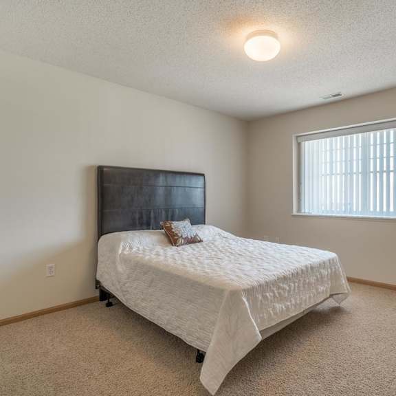 Thumbnail 11 of 20 A bedroom with a bed, a window with blinds, and a wooden headboard.
