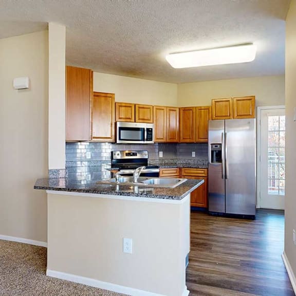 Thumbnail 9 of 28 a kitchen featuring wooden cabinets, granite countertops, a peninsula, a tile backsplash, hardwood floors, and stainless steel appliances