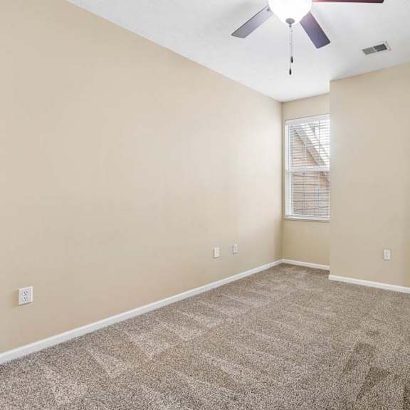 Thumbnail 17 of 34 Bright, empty apartment bedroom with beige walls, carpet, ceiling fan, and window with blinds.