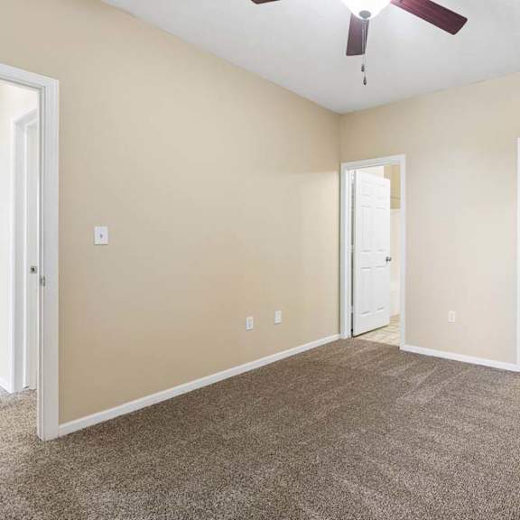 Thumbnail 16 of 34 Carpeted apartment bedroom with beige walls, ceiling fan, and open doorways to nearby rooms.