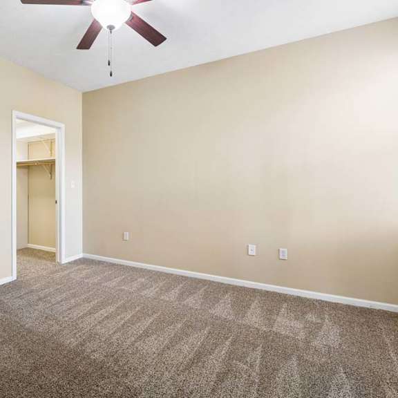 Thumbnail 14 of 34 Empty apartment bedroom with plush carpet, ceiling fan, and open access to bathroom and walk-in closet.