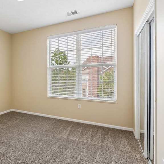 Thumbnail 18 of 34 Bright apartment bedroom with large window, beige walls, carpet, and mirrored closet doors.