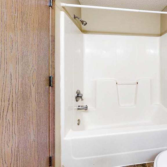 Thumbnail 20 of 31 Full bathroom with white tub and shower surround, chrome fixtures, and adjacent toilet in a neutral interior.