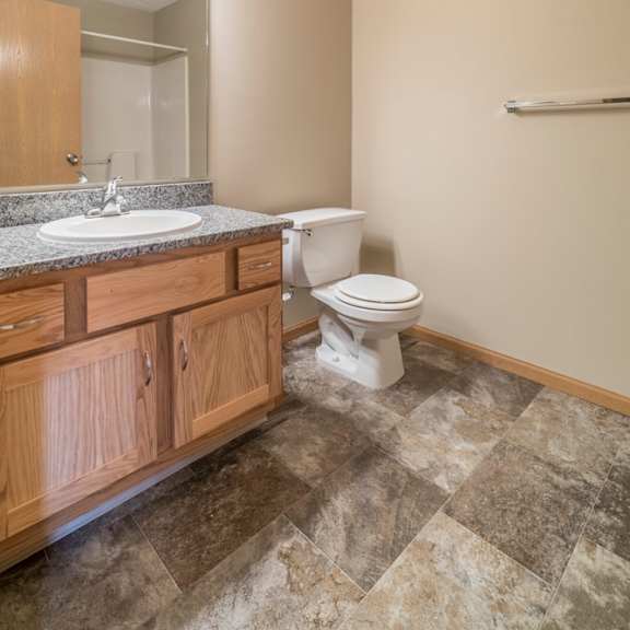 Thumbnail 9 of 12 A bathroom with a toilet, sink, and wooden cabinets.