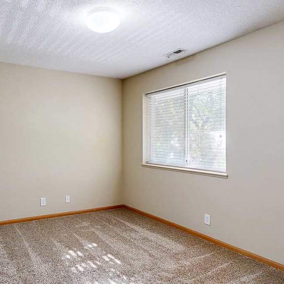 Thumbnail 11 of 22 Bright bedroom with beige walls, plush carpet, wood trim, and a large window with blinds bringing in natural light.