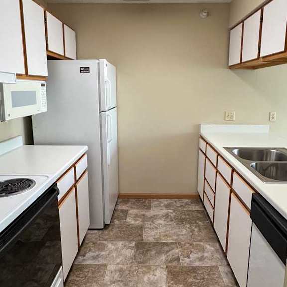 Thumbnail 3 of 9 a kitchen with white and brown cabinets, white appliances, and vinyl flooring