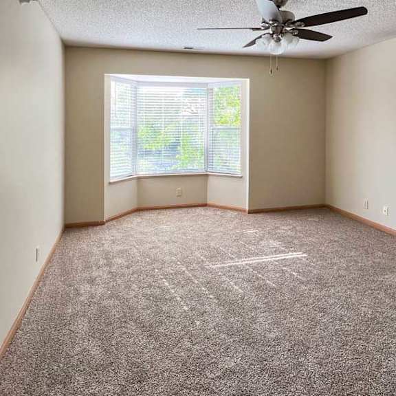 Thumbnail 5 of 9 a carpeted living room with a ceiling fan and a large bay-style window