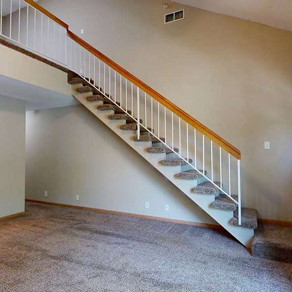 Thumbnail 19 of 27 Open living room with carpeted staircase, white railing, and view toward the kitchen and breakfast bar.