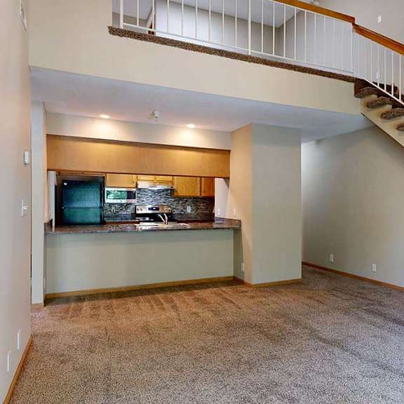 Thumbnail 12 of 27 Spacious living room with loft overlook, carpet flooring, and open kitchen with breakfast bar.