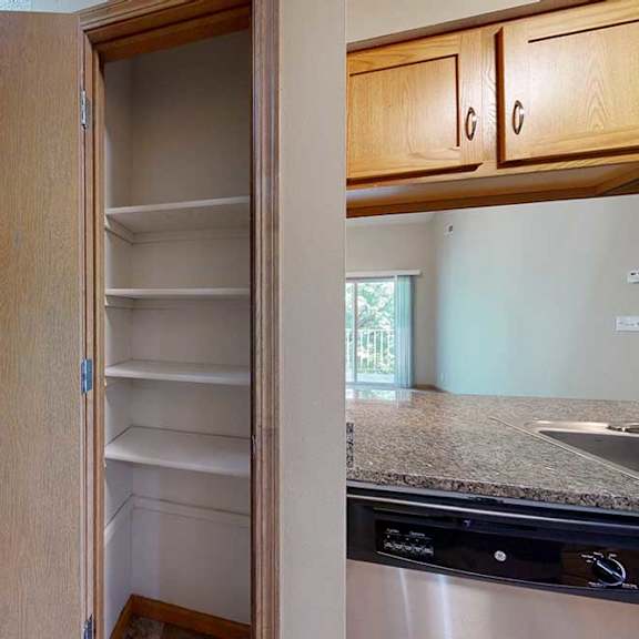 Thumbnail 8 of 27 Built-in pantry closet with multiple white shelves, located beside the kitchen with granite-style countertop and dishwasher.