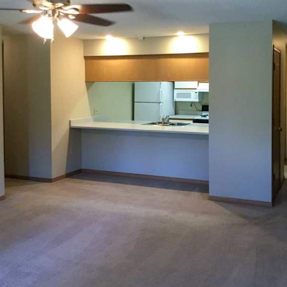 Thumbnail 2 of 11 a living room with a ceiling fan and kitchen with a windowed countertop