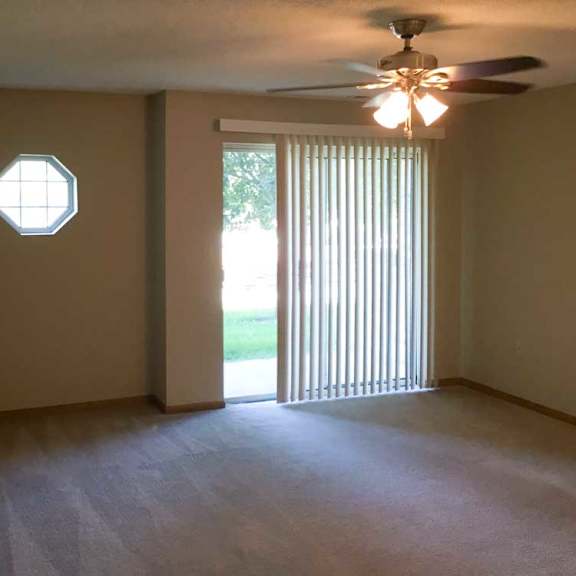 Thumbnail 5 of 11 a living room with a ceiling fan, a sliding glass door with vertical blinds, and a window