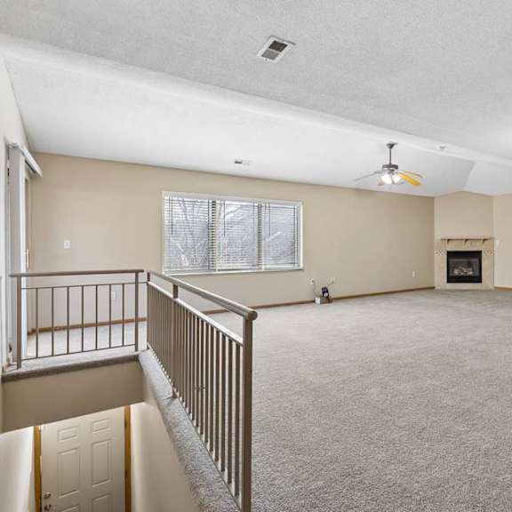 Thumbnail 7 of 17 Spacious upper-level living area with carpeted floors, railing overlook, and fireplace.
