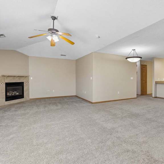 Thumbnail 2 of 17 Carpeted living room with fireplace, ceiling fan, and kitchen view.