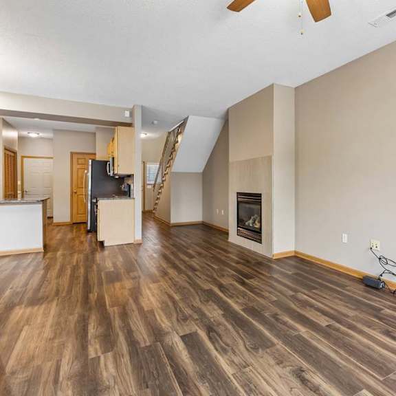 Thumbnail 26 of 29 Open living room with wood-style flooring, gas fireplace, staircase, and adjacent kitchen.