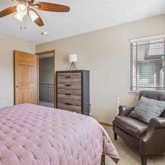 Thumbnail 21 of 29 Apartment bedroom with neutral carpet, ceiling fan, dresser, and large bed in a bright, comfortable setting.