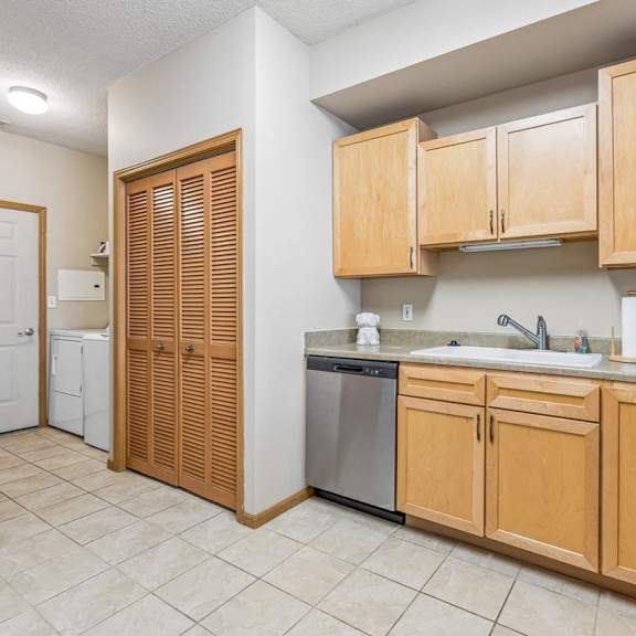 Thumbnail 11 of 29 Functional apartment kitchen with light wood cabinetry, laminate countertops, tile flooring, and dishwasher.