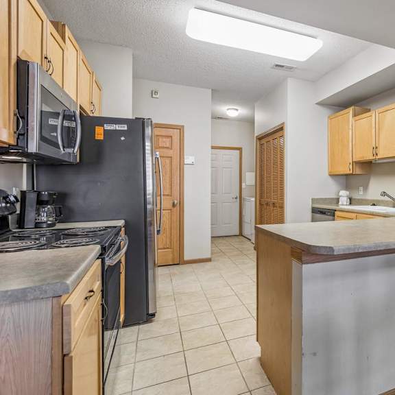 Thumbnail 9 of 29 Open apartment kitchen featuring light wood cabinetry, breakfast bar, tile flooring, and ample prep space.