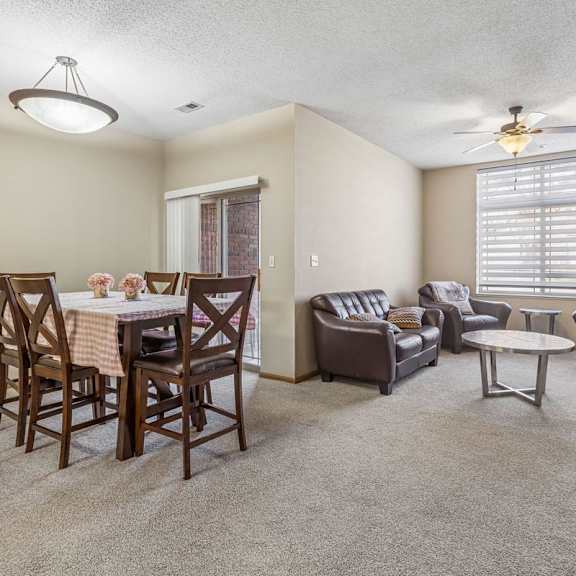 Thumbnail 6 of 29 Spacious apartment living and dining area with neutral carpet, large window with blinds, ceiling fan, and sliding glass door leading to a patio.