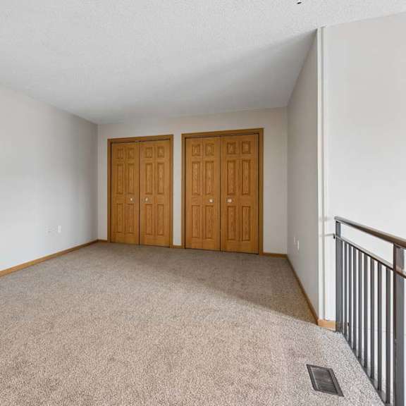 Thumbnail 11 of 18 Carpeted upper-level room with railing overlook and double closet doors.