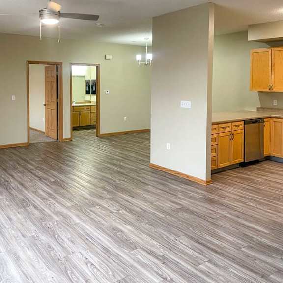 Thumbnail 5 of 18 a living room with a corner fireplace, luxury vinyl tile flooring, and a ceiling fan next to a kitchen