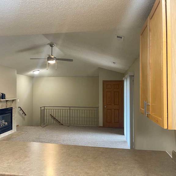 Thumbnail 11 of 21 a living room with a fireplace, a ceiling fan, and a metal railing over some stairs
