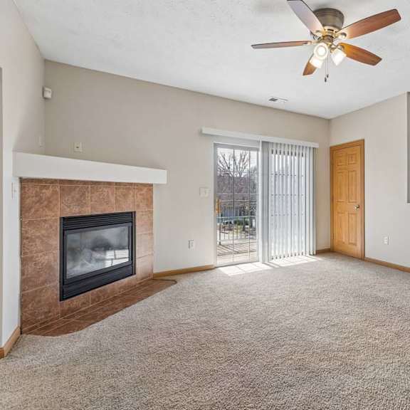 Thumbnail 17 of 19 Bright apartment living room with beige carpet, tiled fireplace, ceiling fan, and sliding glass doors leading to a balcony.