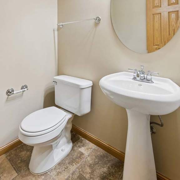 Thumbnail 13 of 17 Half bathroom with pedestal sink, oval mirror, neutral tile flooring, bright vanity lighting, and towel bars.
