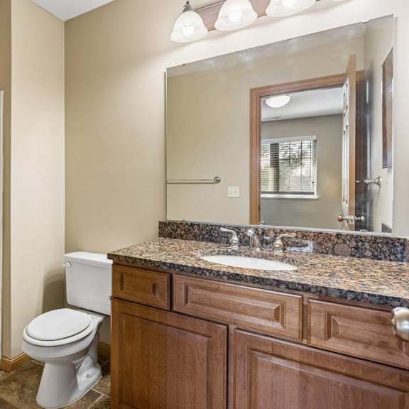 Thumbnail 12 of 17 Bathroom with walk-in shower, wood vanity, speckled countertop, large mirror, and bright vanity lighting.