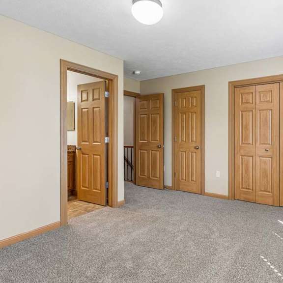 Thumbnail 10 of 17 Empty bedroom with neutral carpet, double closet doors, wood trim, overhead lighting, and direct bathroom access.