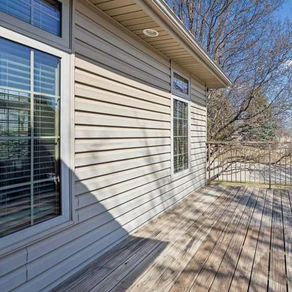 Thumbnail 17 of 17 Spacious outdoor deck with wood plank flooring, metal railing, exterior siding, and views of trees and the community drive.