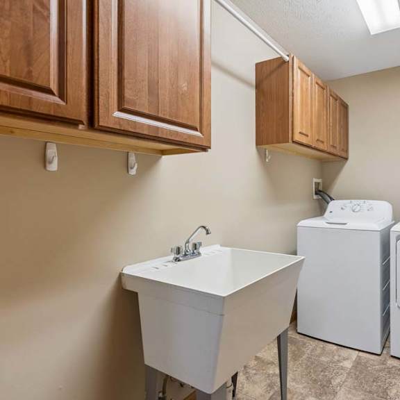 Thumbnail 8 of 17 Laundry room with washer and dryer, utility sink, wood storage cabinets, tile flooring, and overhead lighting.