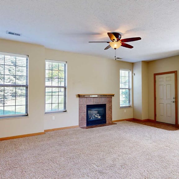 Thumbnail 3 of 28 a living room with a fireplace, a ceiling fan, several tall windows, and a front door