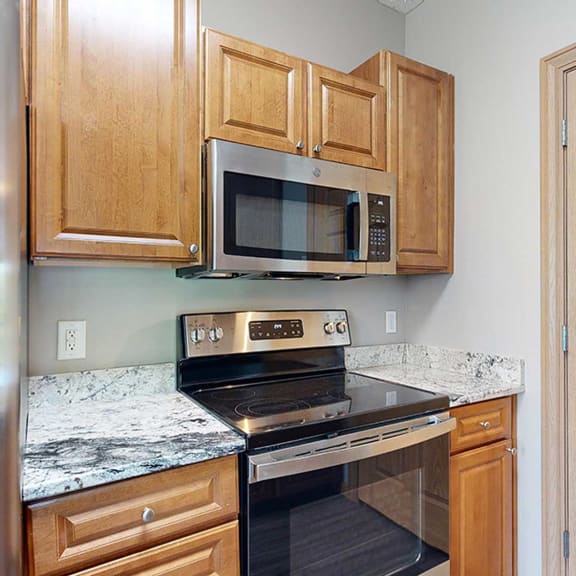 Thumbnail 7 of 24 a kitchen with a stove and microwave and wooden cabinets and a granite countertop