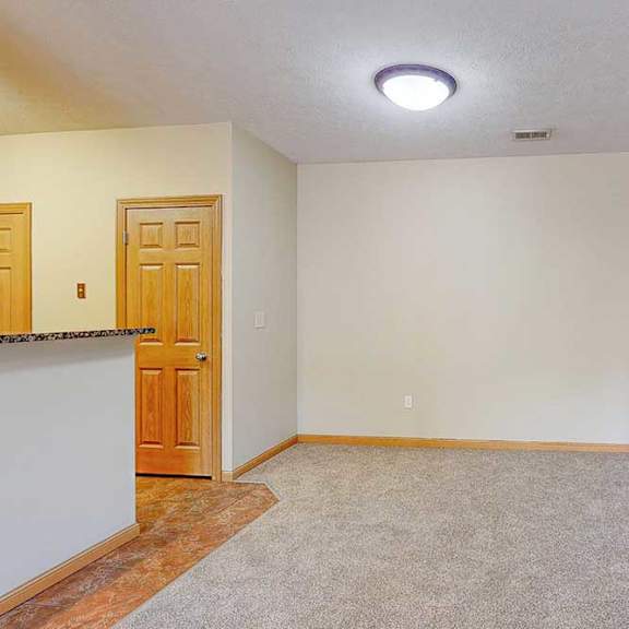 Thumbnail 5 of 31 A carpeted living room next to a kitchen and an open area for a dining room set up.