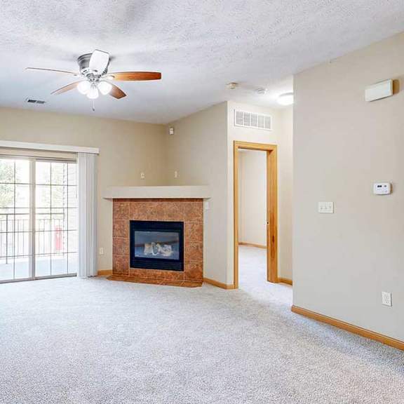 Thumbnail 13 of 31 A living room with a fireplace, a ceiling fan, a built-in desk, and a sliding glass door.