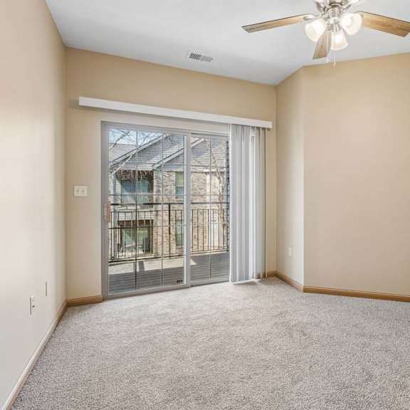 Thumbnail 27 of 31 Bright apartment bedroom with neutral carpeting, a ceiling fan, and sliding glass doors opening to a private balcony.