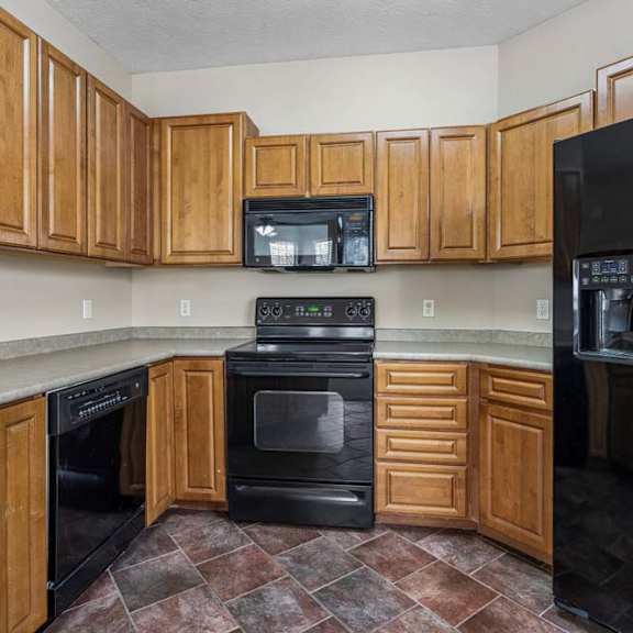 Thumbnail 24 of 31 U-shaped apartment kitchen with extensive wood cabinetry, wraparound counters, black appliances, and a double-basin sink.