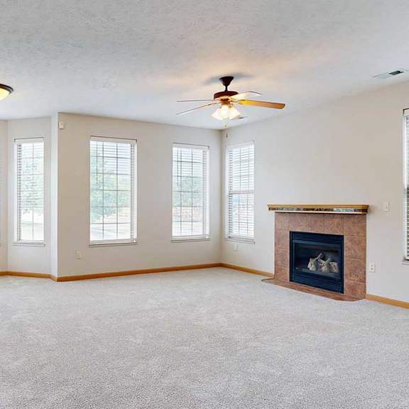 Thumbnail 9 of 39 A living room with a tiled fireplace, a bay window, several other tall windows for plenty of natural light, and a ceiling fan light.